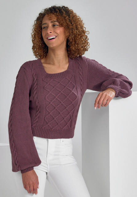Picture shows a Lady in a Long sleeve sweater. The sweater has floppy 'bell' ends and a tight cuff. There is a criss cross cabled panel on front and twist cables down sleaves and each side of panel.